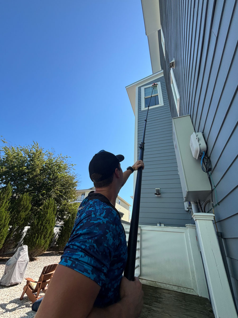 man with rose property services using an extension tool to reach and clean second story windows outside